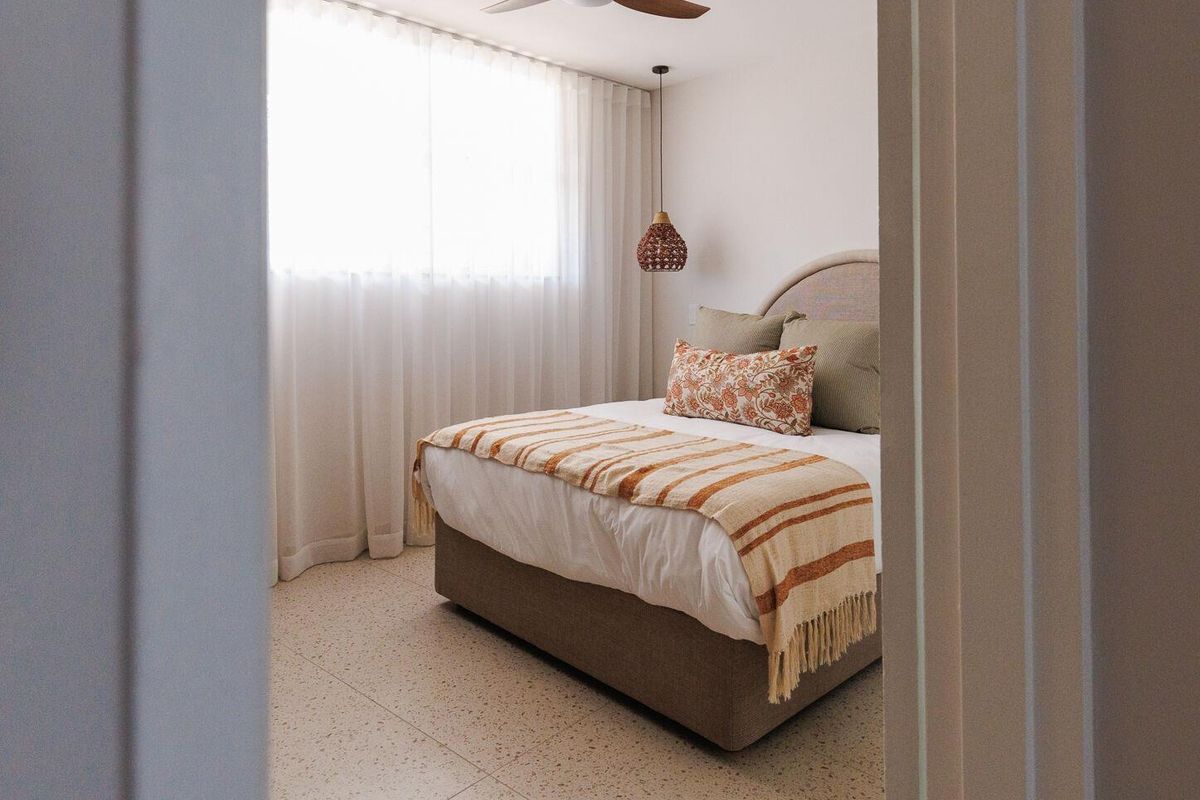 A well-lit bedroom featuring modern terrazzo flooring, a ceiling fan, and elegant pendant lighting, viewed through a doorway.