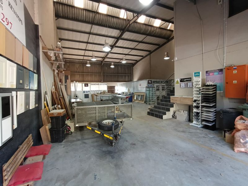 Spacious industrial workshop area featuring high ceilings with exposed steel trusses, concrete flooring, and dedicated zones for sanding and spray booth operations.
