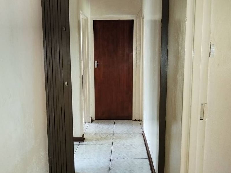 A functional hallway featuring tiled flooring and a wooden door, showing signs of wear on the wall surfaces.
