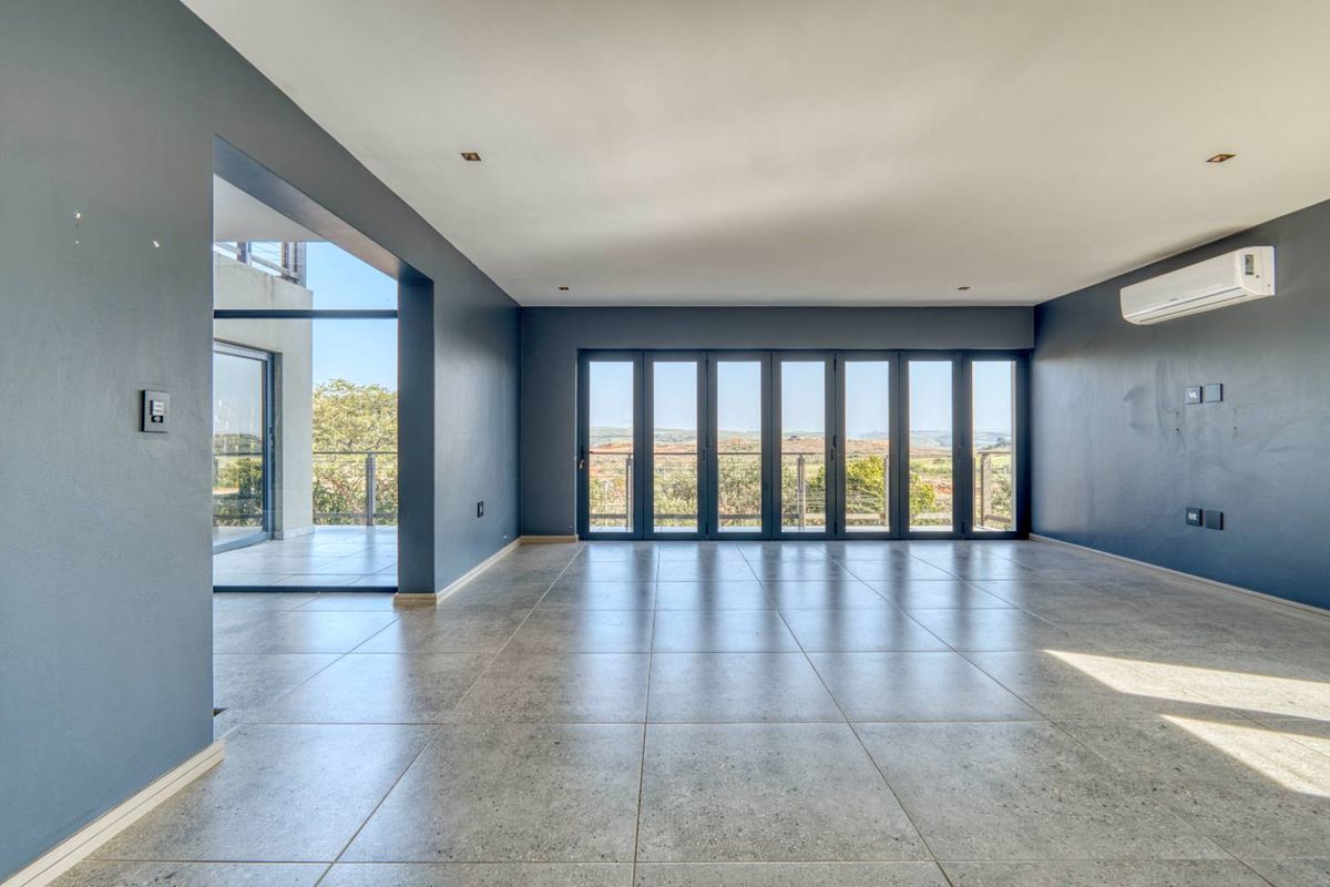 Spacious, empty living area featuring large stacking glass doors that open to a balcony, tiled floors, and a wall-mounted air conditioning unit.