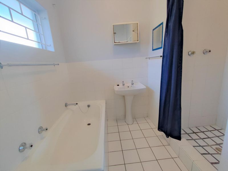 A functional bathroom featuring a pedestal basin, built-in bathtub, and a separate shower area with white tiled finishes.