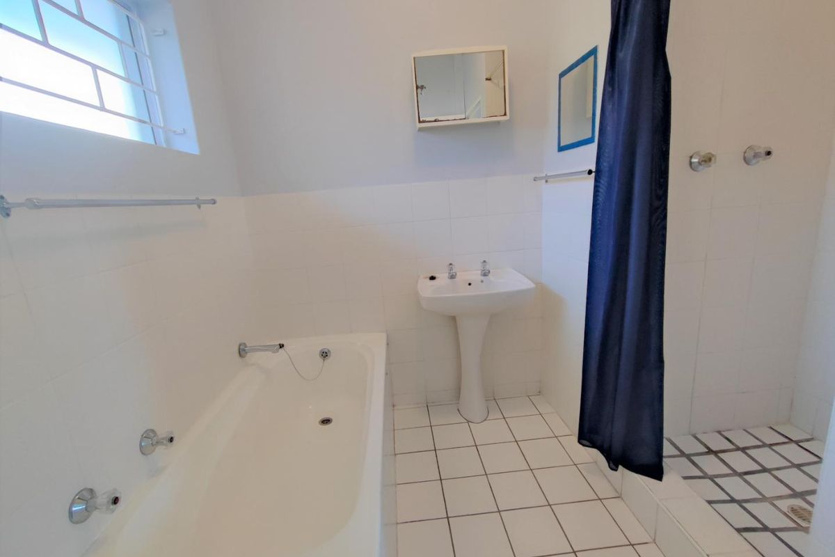 A functional bathroom featuring a pedestal basin, built-in bathtub, and a separate shower area with white tiled finishes.