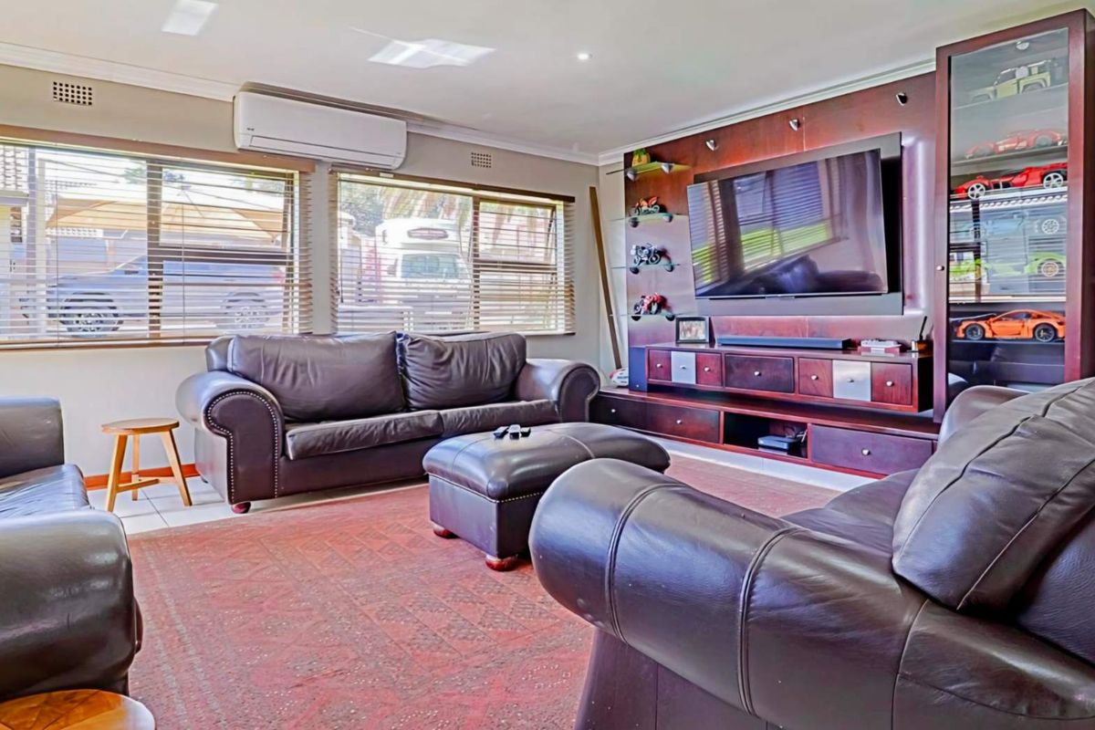 A comfortable living room featuring a large built-in dark wood entertainment unit, split-system air conditioning, and large windows with venetian blinds.