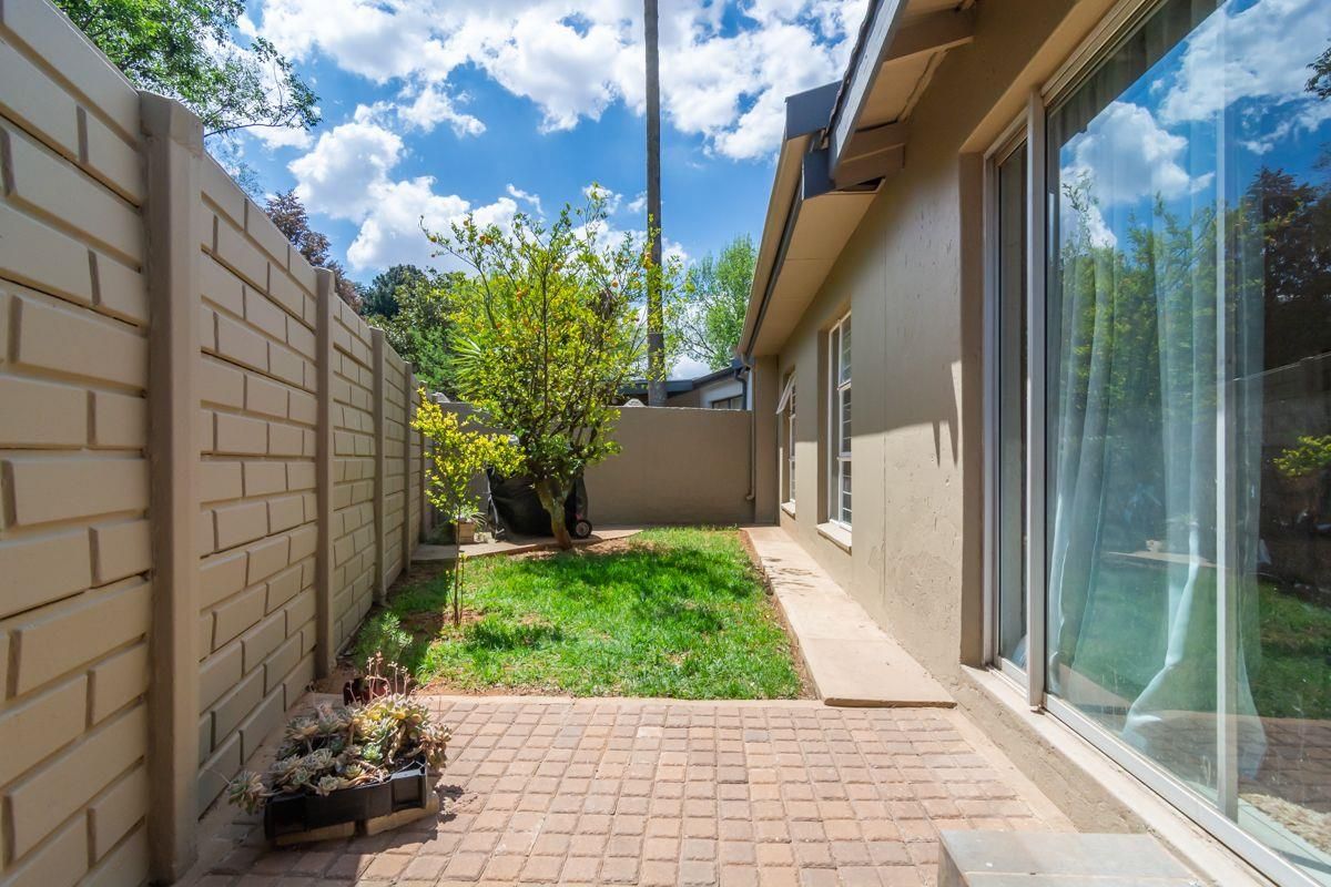 A private rear garden featuring a paved patio area, a small lawn, and perimeter boundary walls, accessible via sliding glass doors.