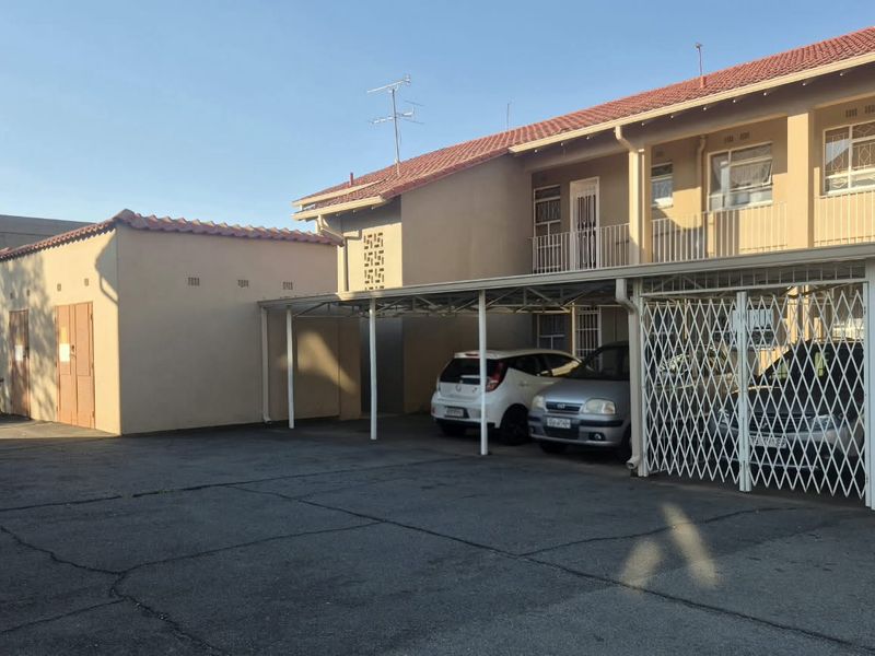 Exterior view of the townhouse complex featuring a paved driveway, covered carport parking, and security gates.