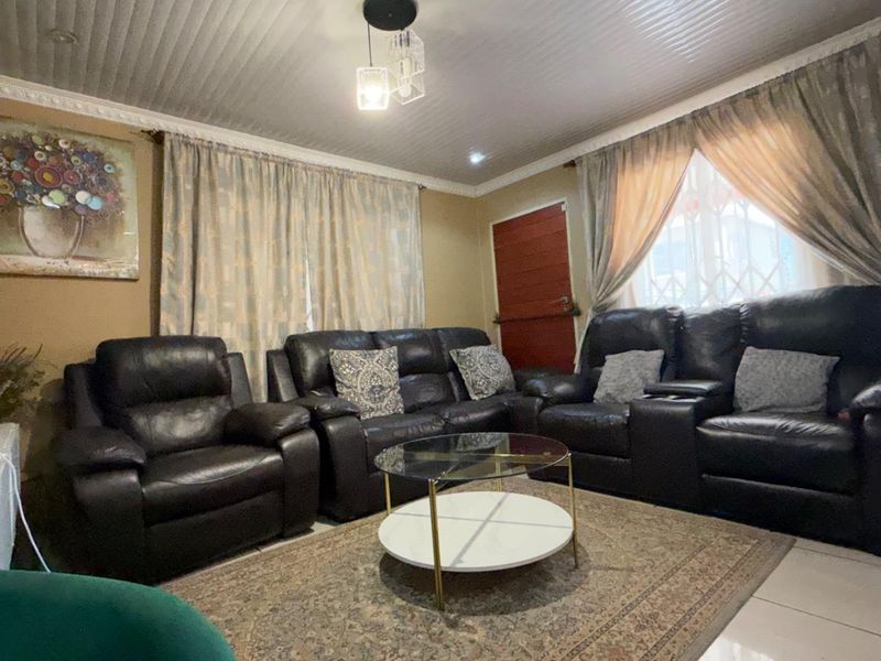 A comfortable living room featuring tiled flooring, a beaded ceiling with decorative cornice, and a secure entrance door.