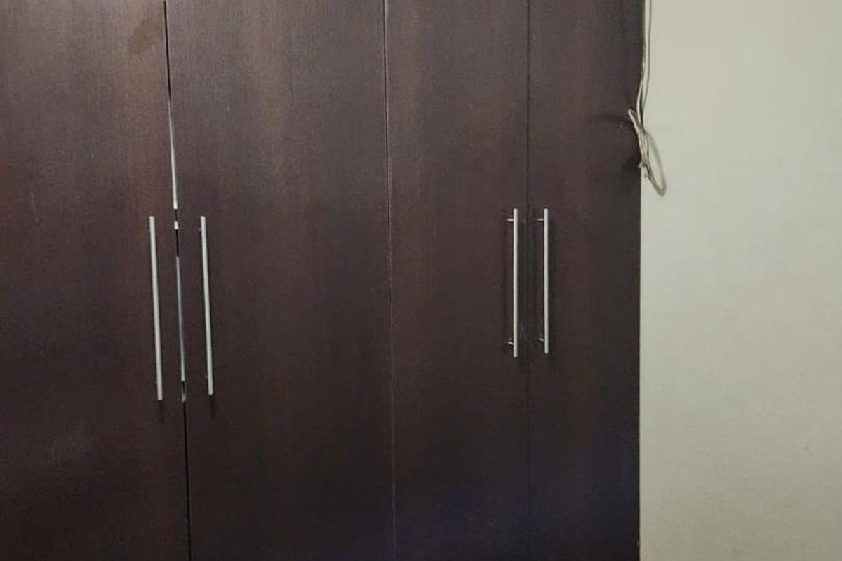 A bedroom featuring dark wood built-in wardrobes with modern handles, ceiling cornice detailing, and tiled flooring.