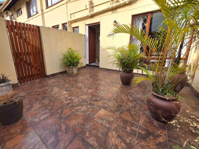 A private paved patio area featuring tiled flooring, a wooden privacy screen, and direct access to the interior through a timber-framed glass door.