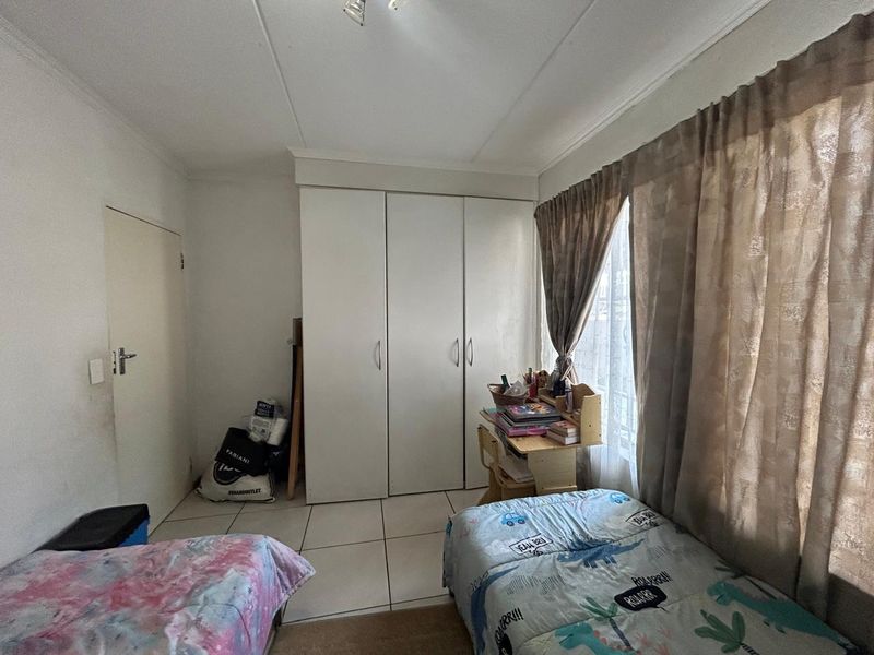 A functional bedroom featuring tiled flooring, a built-in wardrobe, and natural light through a window with curtains.