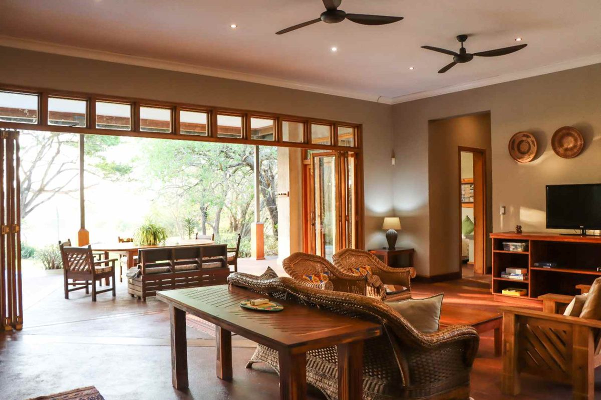 Spacious living area featuring polished concrete floors, ceiling fans, and large bi-fold timber doors opening onto a covered patio with natural bushveld views.