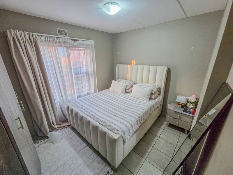 A compact bedroom featuring tiled flooring, a built-in cupboard, and a window with curtain treatments.