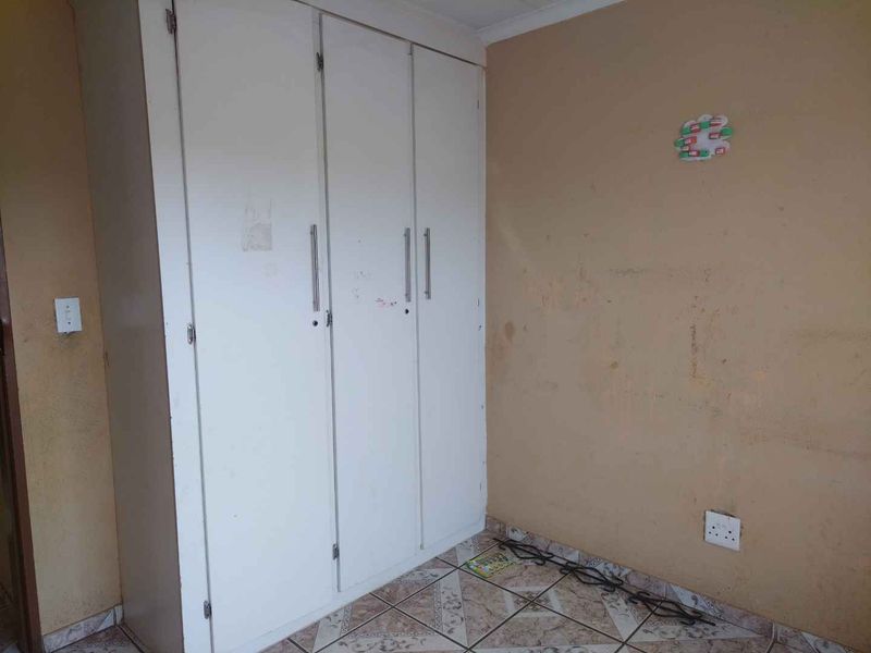 A bedroom featuring a built-in wardrobe and tiled flooring, requiring cosmetic updates to the wall finishes.
