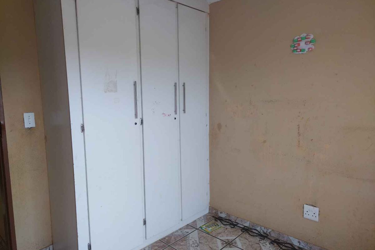 A bedroom featuring a built-in wardrobe and tiled flooring, requiring cosmetic updates to the wall finishes.