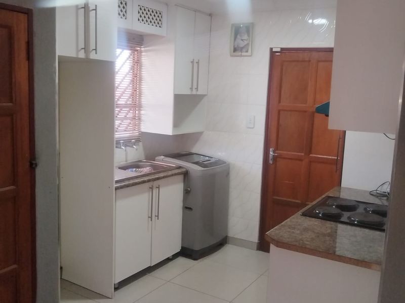 Compact kitchen featuring white cabinetry, laminate countertops, an integrated electric hob, and tiled flooring with dedicated space for laundry appliances.