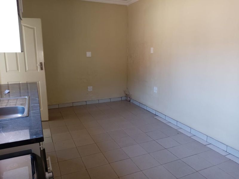 An empty kitchen area featuring tiled flooring, a countertop with a sink, and visible wall wear requiring maintenance.