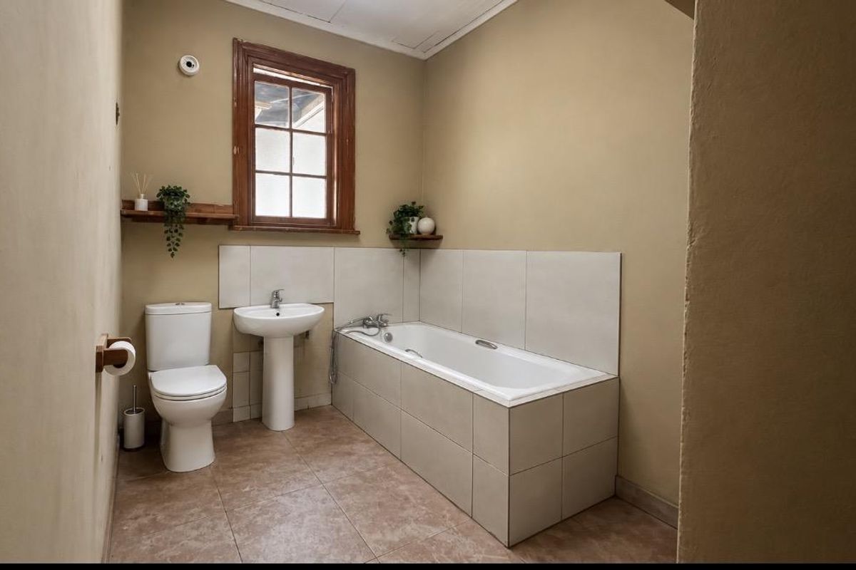 A functional bathroom featuring a pedestal basin, toilet, and a tiled bathtub with a wooden window frame.