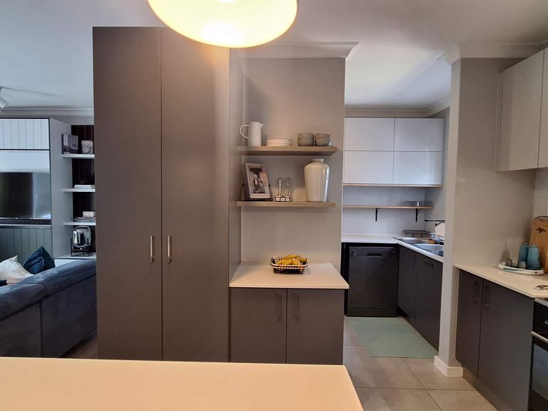 Modern open-plan kitchen and living area featuring sleek grey cabinetry, built-in appliances, tiled flooring, and functional storage solutions.