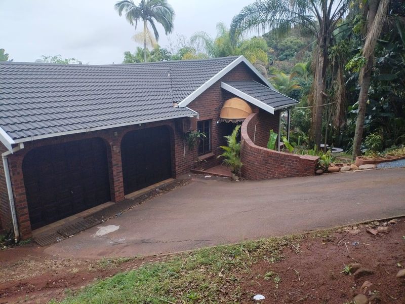 Front exterior view of a brick house featuring a double garage, curved brick retaining wall, and an asphalt driveway set in a landscaped garden.
