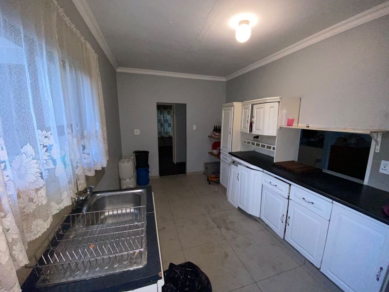 A functional kitchen featuring white built-in cabinetry, dark laminate countertops, a stainless steel sink, and tiled flooring, offering potential for modern updates.