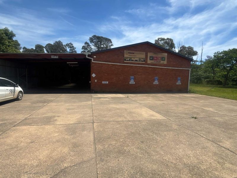 Industrial property exterior featuring a large concrete driveway, brick facade, and a covered loading bay area.