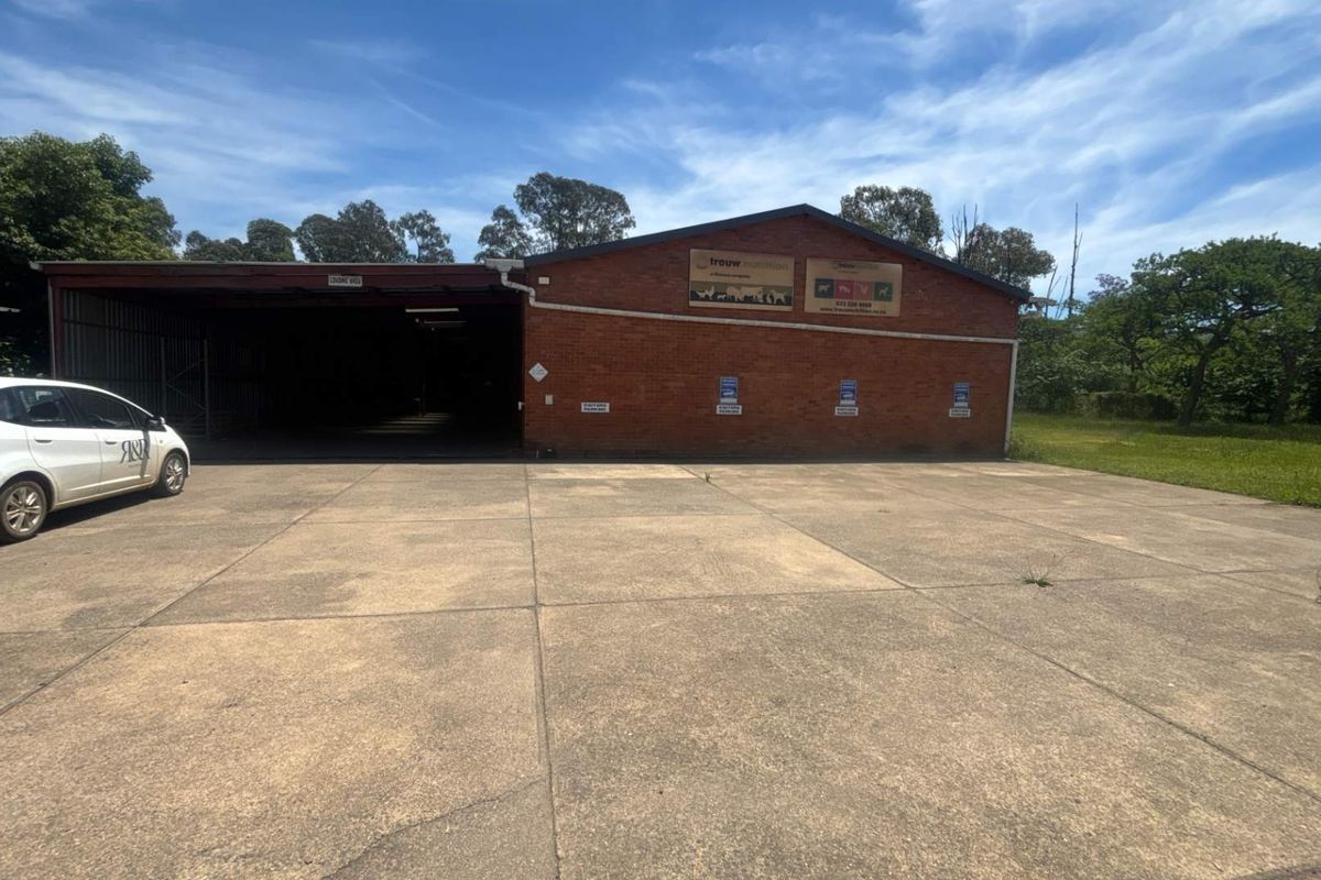 Industrial property exterior featuring a large concrete driveway, brick facade, and a covered loading bay area.