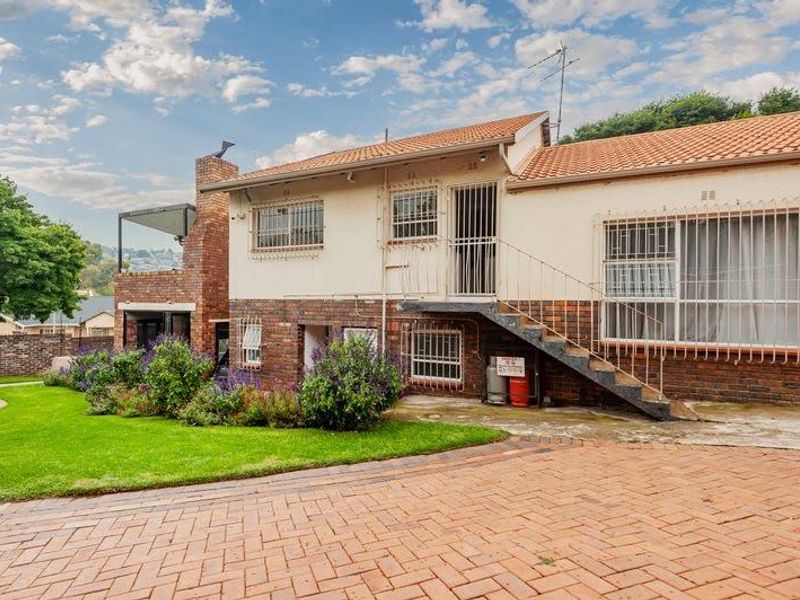 Rear view of the property featuring a brick facade, external staircase, security bars, and a paved driveway leading to a landscaped garden area.