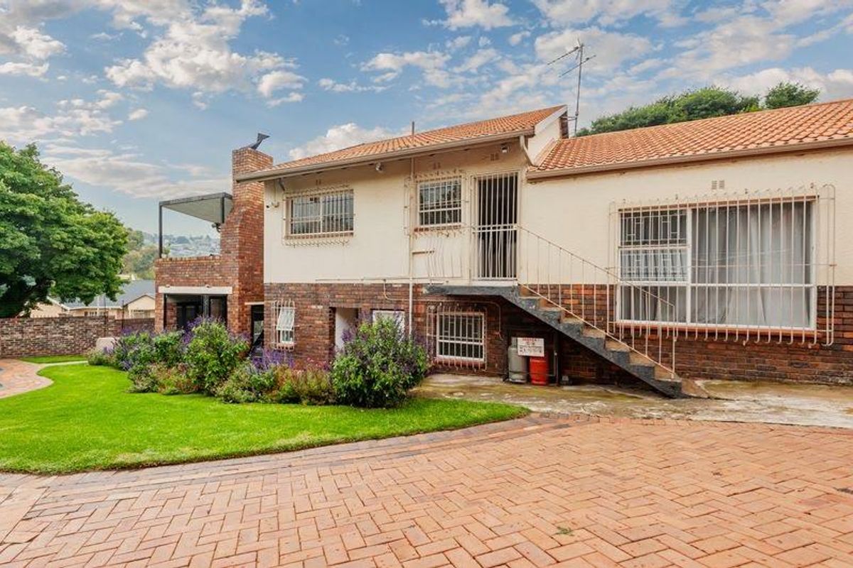 Rear view of the property featuring a brick facade, external staircase, security bars, and a paved driveway leading to a landscaped garden area.