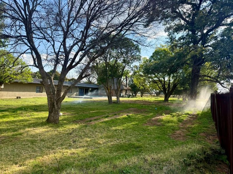 Spacious farm garden featuring mature trees, an active irrigation system, and established perimeter fencing, offering a natural outdoor setting.