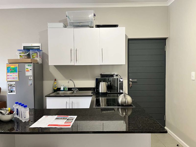 Compact kitchen area featuring granite countertops, white cabinetry, a stainless steel sink, and a built-in hob, providing a functional and modern workspace.