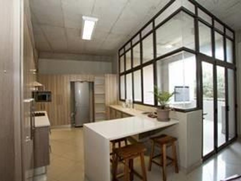 Modern kitchen featuring light wood cabinetry, stone countertops, a breakfast bar, and a contemporary glass partition wall with an exposed concrete ceiling.