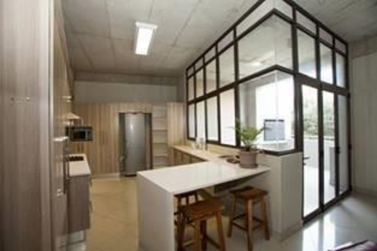 Modern kitchen featuring light wood cabinetry, stone countertops, a breakfast bar, and a contemporary glass partition wall with an exposed concrete ceiling.
