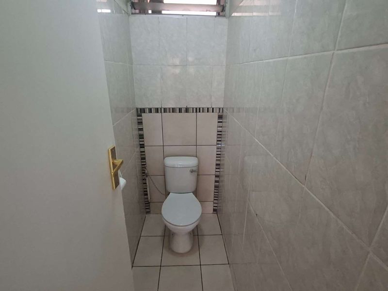 A compact, tiled guest toilet featuring neutral ceramic wall and floor tiles with a decorative accent border.
