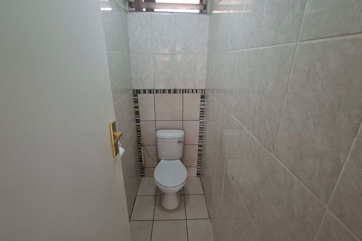 A compact, tiled guest toilet featuring neutral ceramic wall and floor tiles with a decorative accent border.