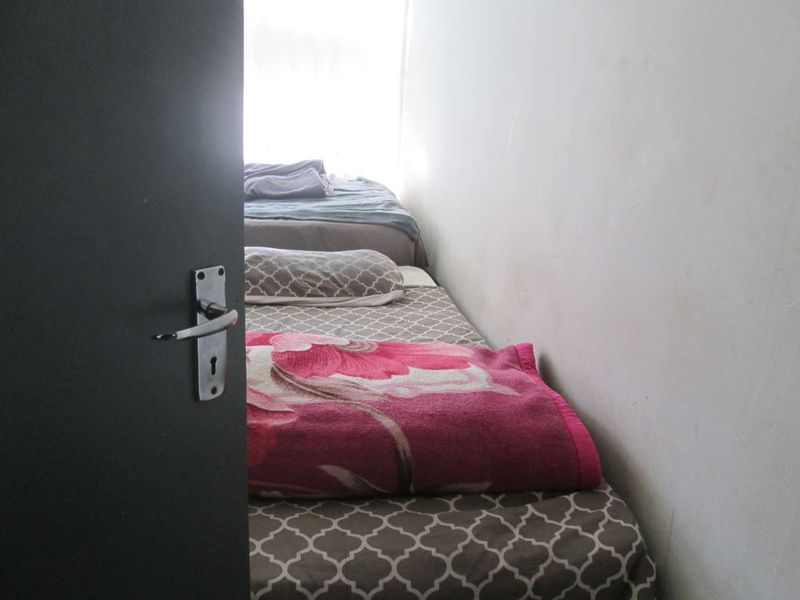 A narrow bedroom space featuring plain walls and a doorway entrance.