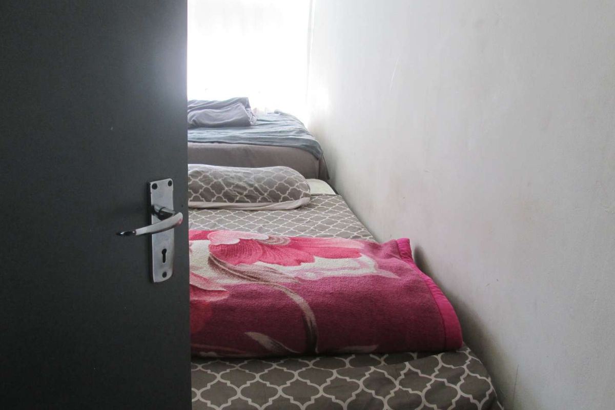 A narrow bedroom space featuring plain walls and a doorway entrance.