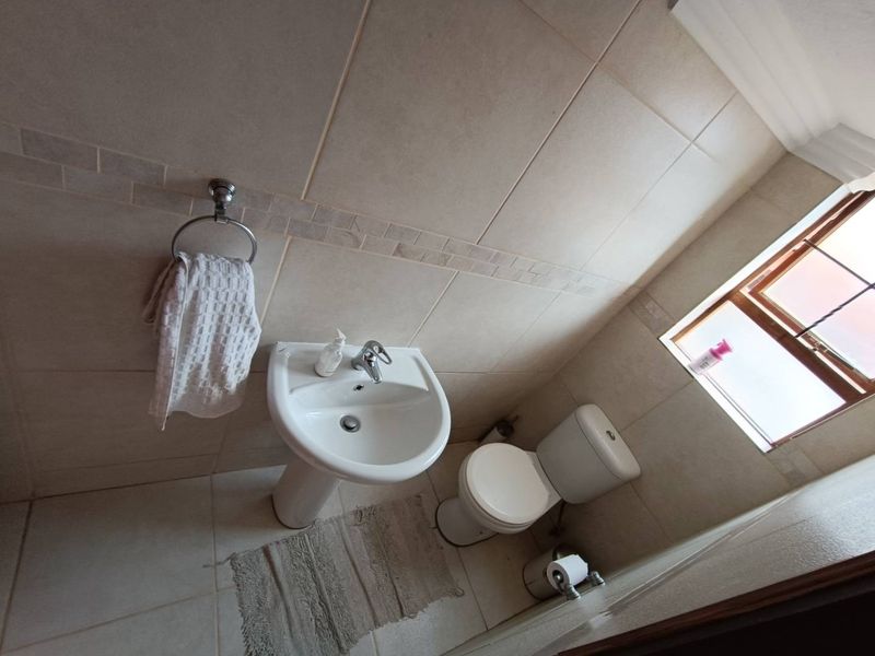 A compact bathroom featuring a pedestal basin, toilet, and neutral floor-to-ceiling wall tiling with a decorative border.