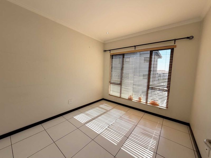 A bright, empty bedroom featuring neutral tiled flooring, large windows with venetian blinds, and clean wall finishes, ready for personalization.