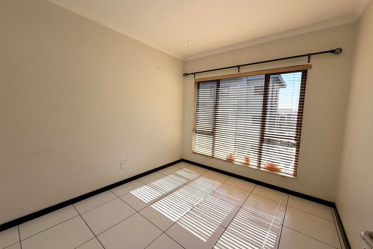 A bright, empty bedroom featuring neutral tiled flooring, large windows with venetian blinds, and clean wall finishes, ready for personalization.