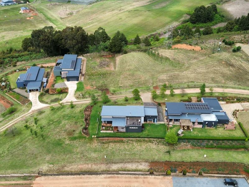 Aerial view of a residential estate featuring multiple modern homes with metal roofs, solar panels, paved driveways, and established landscaped gardens.