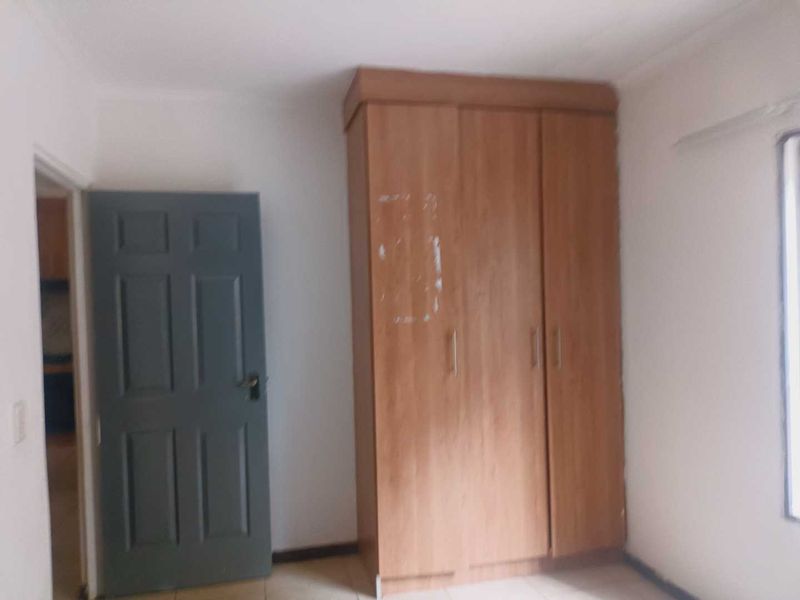 A vacant bedroom featuring a built-in wooden wardrobe and a grey internal door, requiring minor cosmetic updates to improve its overall appeal.