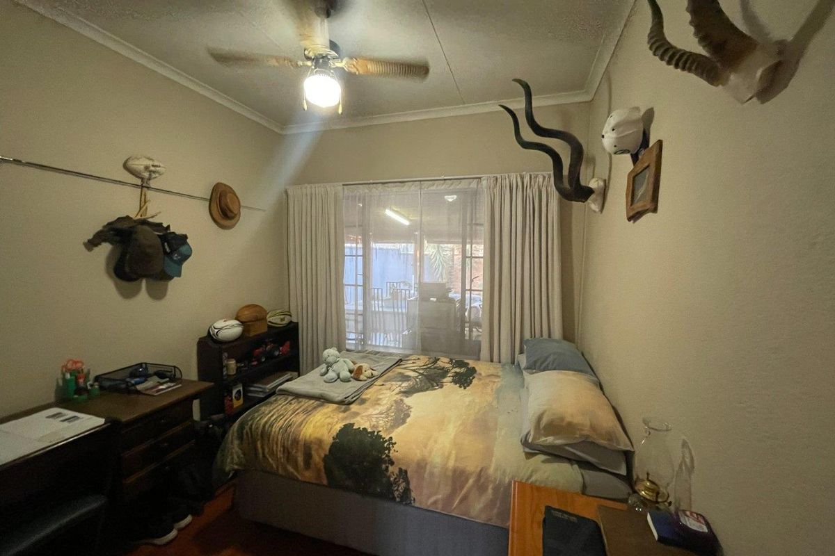 A standard bedroom featuring wooden flooring, a ceiling fan, and large windows with curtains providing natural light and access to the patio area.