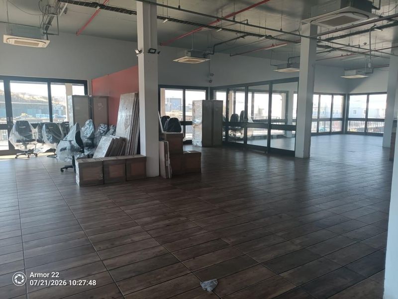 Spacious open-plan retail or office area featuring wood-look tiled flooring, exposed industrial-style ceilings, and extensive glass partitioning for natural light.