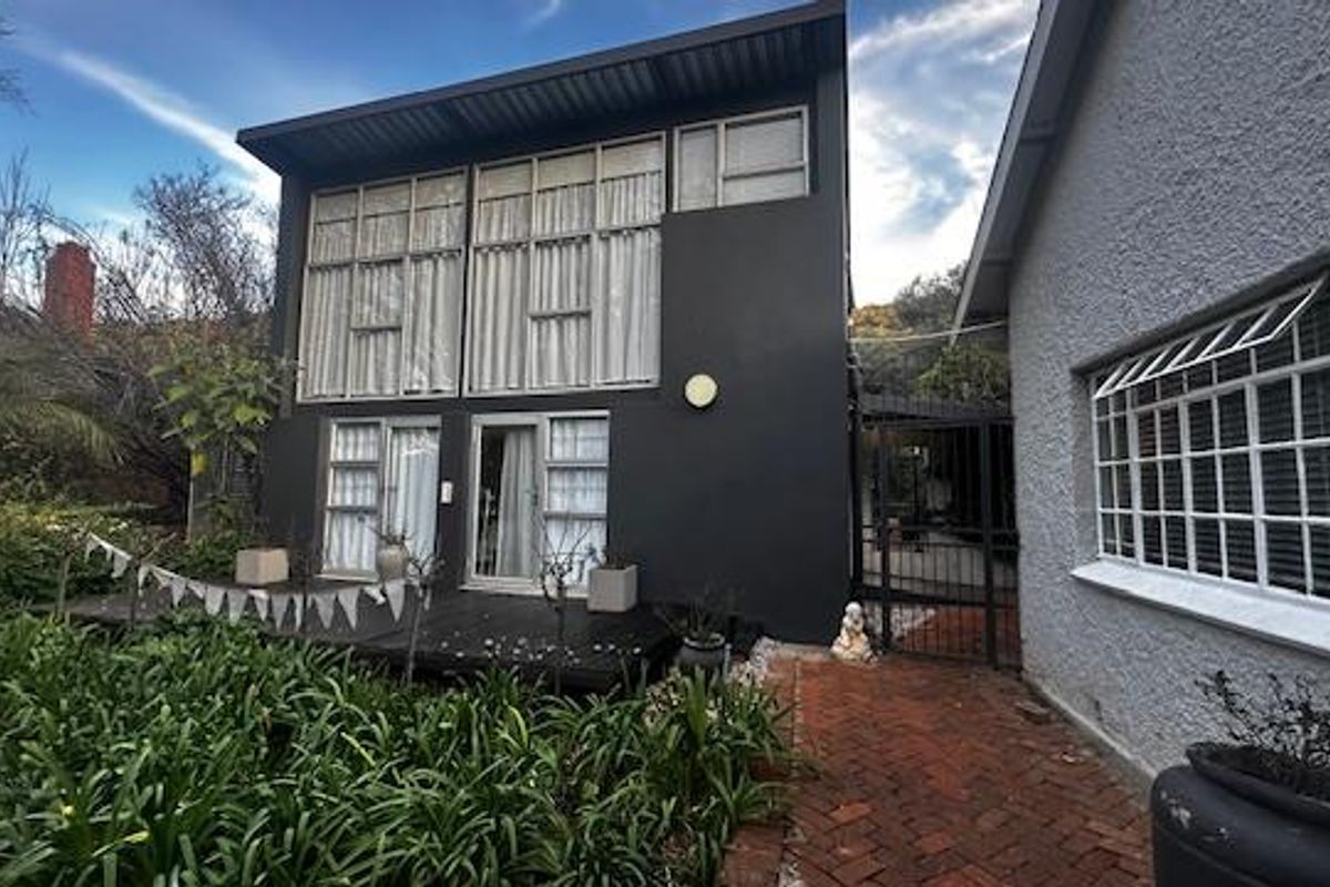 Rear view of the property featuring a modern dark-painted extension with large windows, timber decking, and a brick-paved pathway.