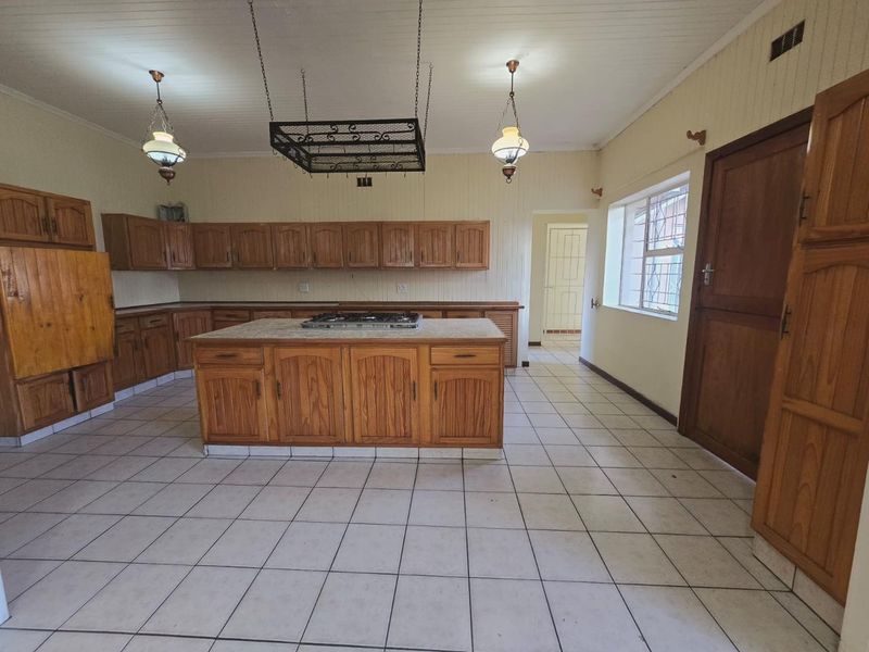 Spacious kitchen featuring extensive wooden cabinetry, a central island with a built-in gas hob, tiled flooring, and a classic timber panelled ceiling.