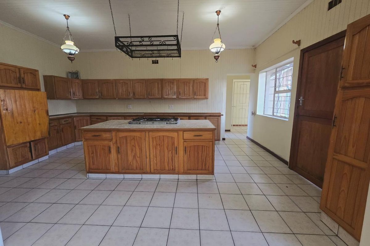 Spacious kitchen featuring extensive wooden cabinetry, a central island with a built-in gas hob, tiled flooring, and a classic timber panelled ceiling.