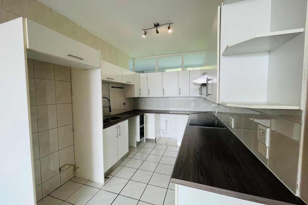 A functional kitchen featuring white cabinetry, dark countertops, tiled flooring, and built-in hob, offering a clean and practical workspace.