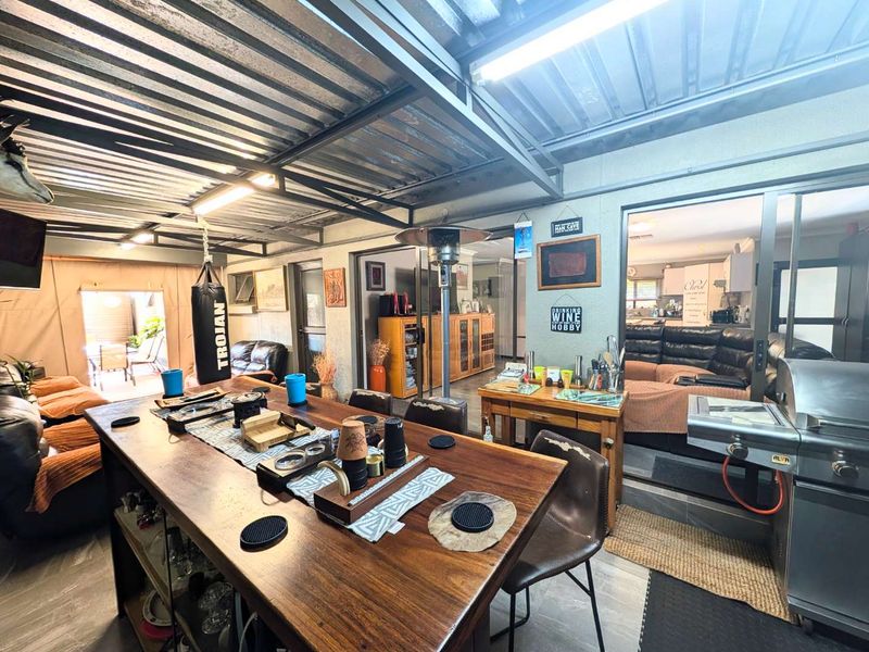 A spacious covered patio area featuring exposed steel beams, corrugated metal roofing, and direct access to the main living area through sliding glass doors.