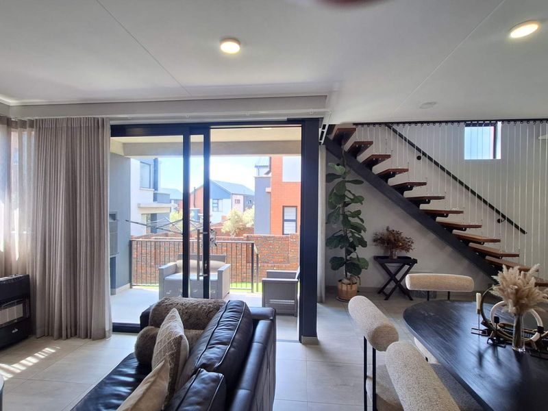 Modern open-plan living area featuring tiled floors, recessed lighting, and a contemporary staircase with timber treads leading to the upper level.