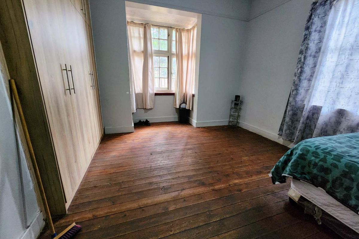 A bedroom featuring polished timber flooring, built-in wooden wardrobes, and a bay window, showing signs of ceiling water damage.