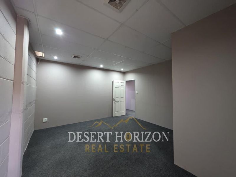 An empty office space featuring a suspended ceiling with recessed lighting, air conditioning vents, and dark carpet flooring.